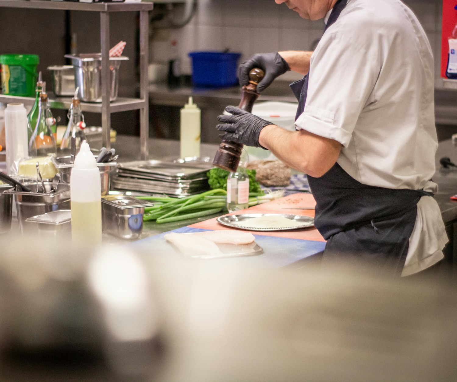 A cook working a prep station in gloves, both hands full