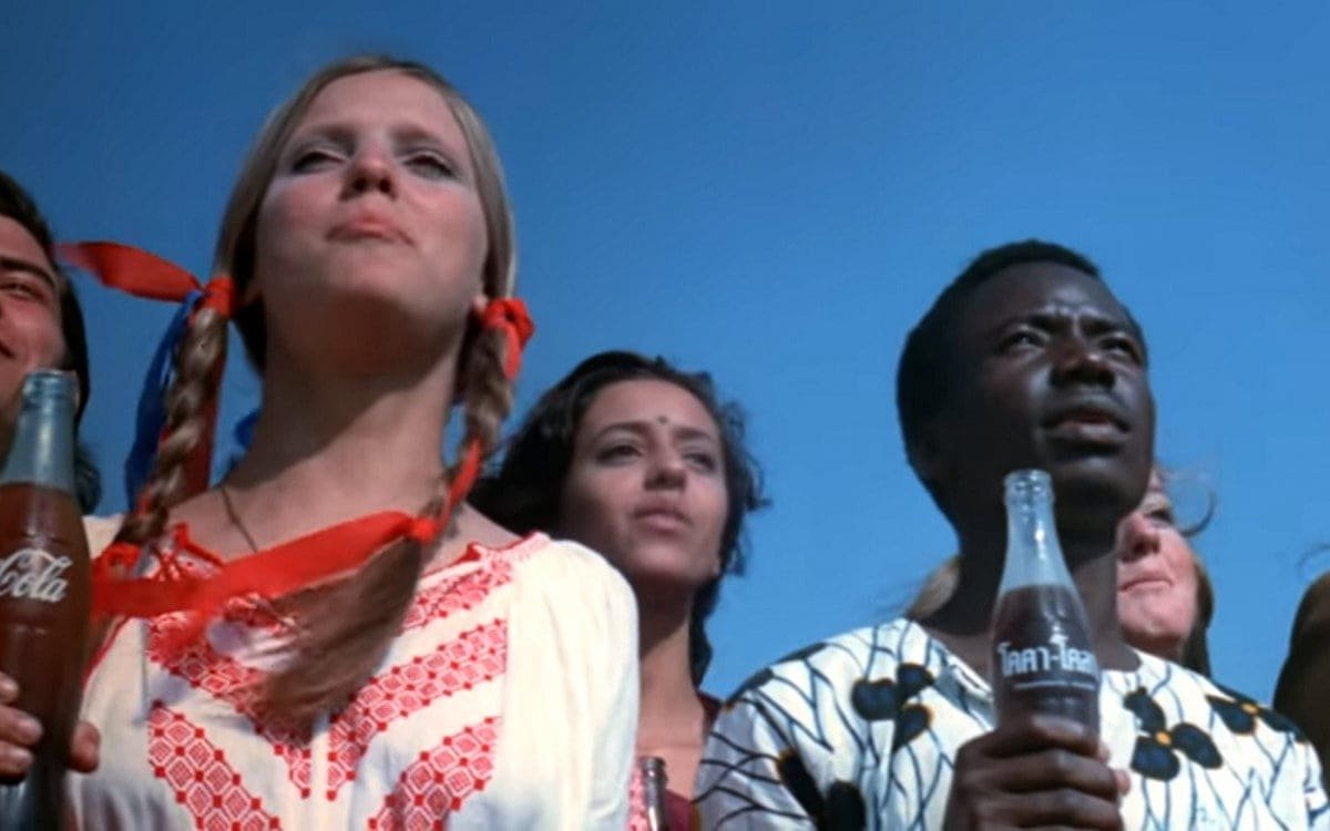 Young people on a hilltop singing and holding Coke bottles